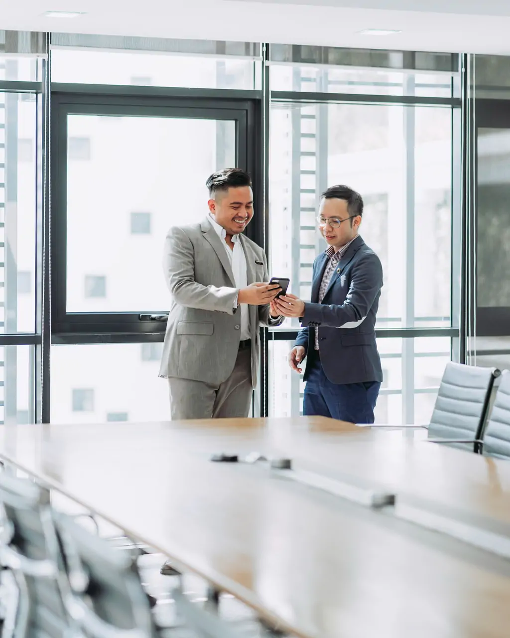 Two businessmen looking at a phone, smiling.